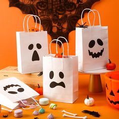 three halloween bags with faces on them and candy in front of an orange wall behind them