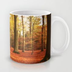 a coffee mug with an image of trees in the fall colors and leaves on the ground