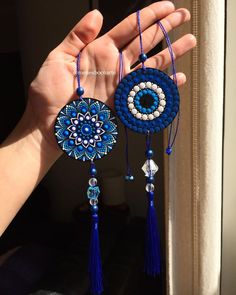 the hand is holding two blue and white beaded necklaces with tassels