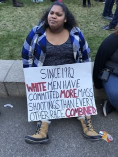 a woman sitting on the ground holding a sign