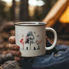 a person holding a coffee mug with trees painted on the front and sides in their hands