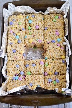 rice krispy treats in a baking pan with aluminum foil on the bottom and colorful candy candies on top