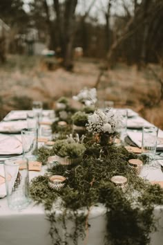 an outdoor table set up with flowers, candles and place settings for a dinner party