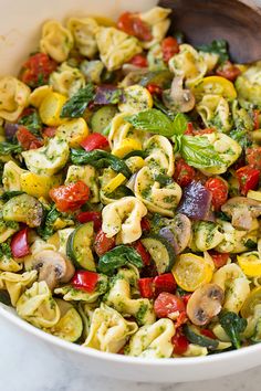 a white bowl filled with pasta salad on top of a table next to a fork