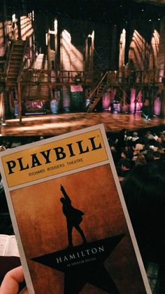 a person holding up a playbill book in front of a stage