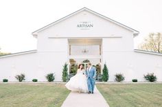 a bride and groom walking out of the front of a white barn with their wedding dress blowing in the wind