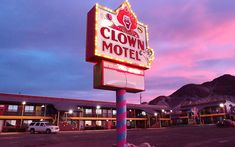 a motel sign lit up at dusk with mountains in the backgrouund and clouds in the sky