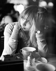 a black and white photo of a woman sitting at a table with a coffee cup