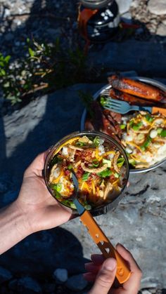 a person holding a spoon in front of a plate of food on a table outdoors