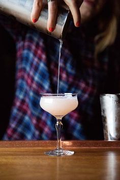 a woman pouring something into a glass on top of a table