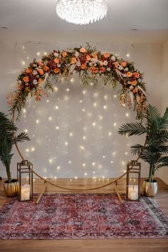 a wedding arch decorated with flowers and greenery on a rug in front of a chandelier