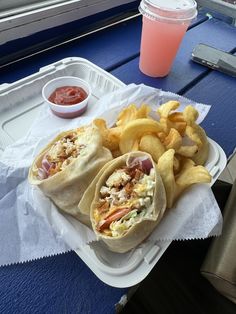 two burritos and french fries on a tray next to a cup of ketchup