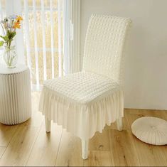 a white chair sitting on top of a wooden floor next to a vase with flowers