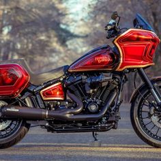 a red and black motorcycle parked on the side of a road in front of trees