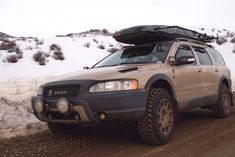 an suv with a surfboard on the roof driving down a snowy road