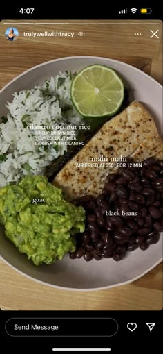 a white plate topped with fish and beans next to a lime wedge on top of rice