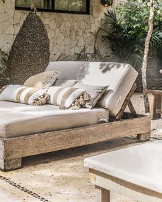 an outdoor daybed made out of wood with pillows on it and some plants in the background