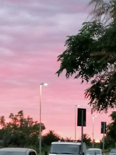 several cars are parked on the side of the road at dusk time, with pink clouds in the background