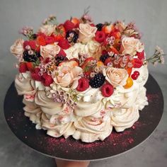 there is a cake with berries and flowers on the top, sitting on a platter