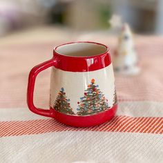 a red and white coffee mug sitting on top of a table next to a small figurine