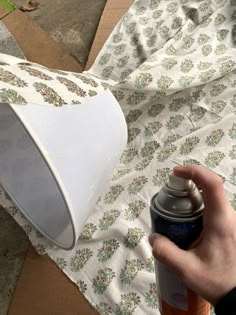 a person holding a spray paint can next to a white lamp on a bed sheet