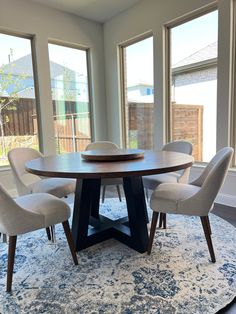 a dining room table with four chairs and a rug in front of the large windows