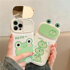 a woman holding two cell phones with frog faces on them, one is green and the other is white