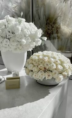 two white vases filled with flowers on top of a table next to a mirror