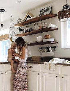 a woman holding a baby in her arms while standing next to a kitchen counter top