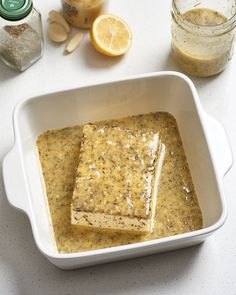 a white bowl filled with food on top of a table next to lemons and seasoning