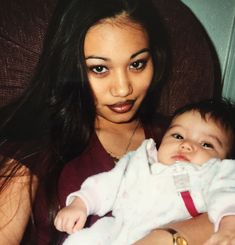 a woman holding a baby in her arms and looking at the camera with an intense look on her face