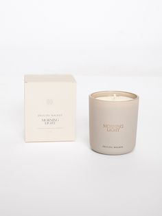 a candle sitting next to a box on a white surface with the words morning light written in it