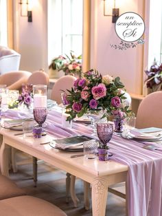 the table is set with purple flowers and place settings