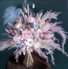 a bouquet of flowers and feathers on top of a wooden table next to a blue wall