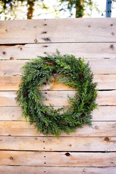 a green wreath on top of a wooden table with pine cones and evergreen branches around it