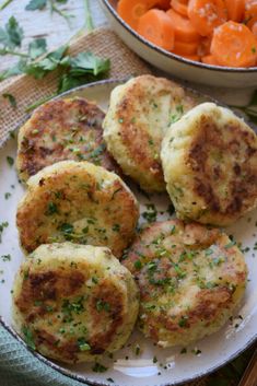 four crab cakes on a plate with carrots and parsley next to it in a bowl