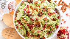 a white bowl filled with lettuce and pomegranate on top of a table