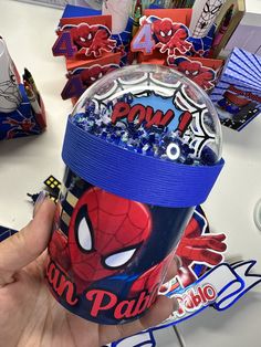 a hand holding up a cup with spiderman decorations on it and candy in the background