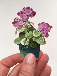 a hand holding a tiny potted plant with purple flowers