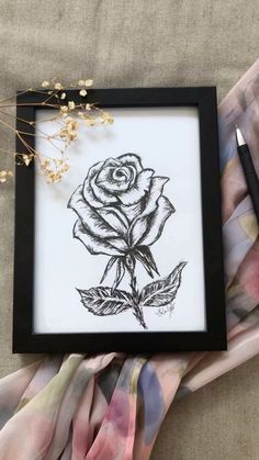 a black and white drawing of a rose in a frame on top of a blanket