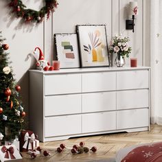 a white dresser with christmas decorations and pictures on it's top, next to a christmas tree