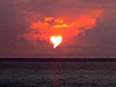 the sun is setting over the ocean with clouds in the shape of a heart on it