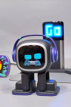 a toy robot with headphones on sitting in front of a cell phone and clock