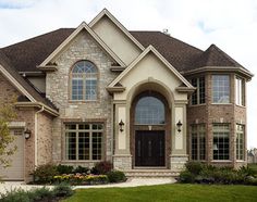 a large brick and stone house with lots of windows on the front door, two car garages to the side