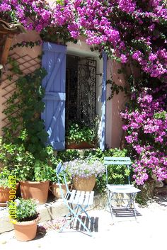 a table and chair sitting in front of a window with purple flowers on the outside