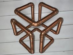 four copper colored metal pipes arranged in the shape of an x on a white wooden floor