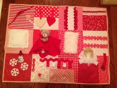 a teddy bear sitting on top of a red and white patchwork quilted blanket