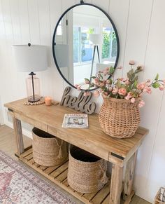 a wooden table topped with baskets filled with flowers next to a round mirror on the wall