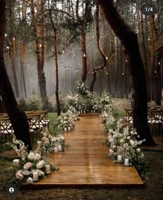 an outdoor wedding setup in the woods with candles and flowers on wooden flooring, surrounded by tall trees