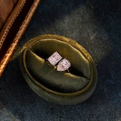 two engagement rings sitting in an old green velvet case on the ground next to a book